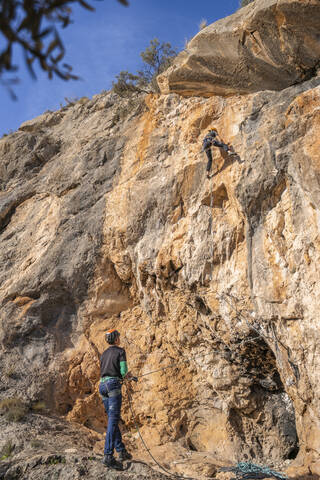 Mann sichert Frau beim Klettern an einer Felswand, lizenzfreies Stockfoto