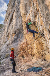 Frau sichert Mann beim Klettern an einer Felswand - DLTSF00450