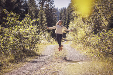 Mädchen läuft und springt auf einem Waldweg und hat Spaß - DHEF00118