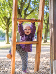 Porträt eines Kleinkindes, das auf dem Spielplatz auf eine Leiter klettert - LAF02458