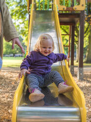 Porträt eines glücklichen Kleinkindes auf einer Rutsche auf einem Spielplatz - LAF02459