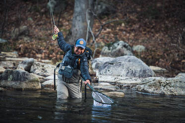 Ein Mann keschert an einem Vormittag an einem Fluss in Maine eine Forelle - CAVF74317