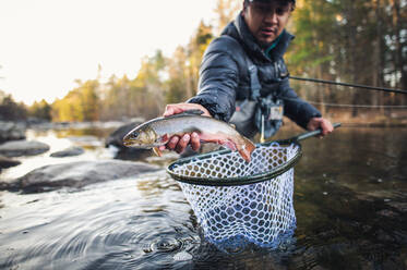 Ein Mann fängt an einem Herbstmorgen in einem Fluss in Maine eine Forelle - CAVF74321