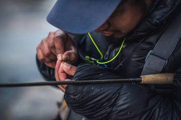 A man ties a fly onto the end of his fishing line on a cold morning - CAVF74327