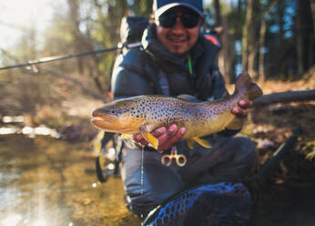 A man catches a large brown trout on a river in Maine - CAVF74345