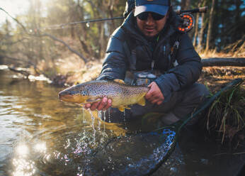 A man catches a large brown trout on a river in Maine - CAVF74348