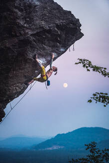 Mann klettert überhängende Sportkletterroute mit Mond. - CAVF74363