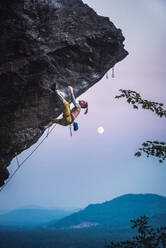 Mann klettert überhängende Sportkletterroute mit Mond. - CAVF74364