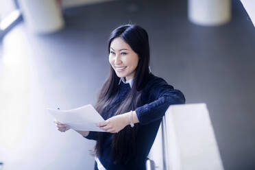 Junge asiatische Frau mit Papier in einem Büro stehend mit Papier - CAVF74494