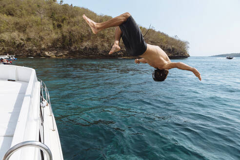 Junger Mann springt von einem Boot, Insel Lembongan, Bali, Indonesien - KNTF04249