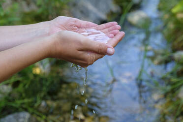 Germany, Hands of young woman drawing water from stream - LBF02878