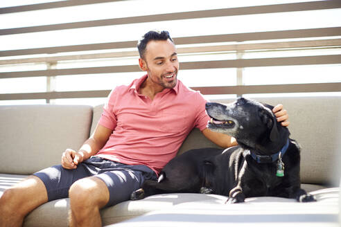 Ein Mann entspannt sich mit seinem Hund auf einer Couch im Freien. - CAVF74535