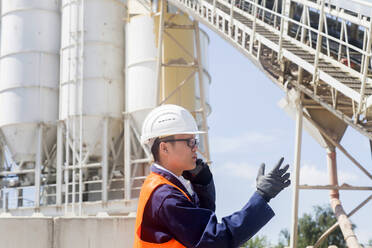 Concrete worker talking to a smart phone in a concrete factory - CAVF74603