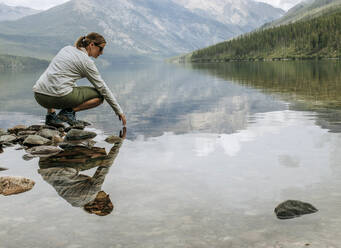 Woman reflected in surface of Kintla Lake surrounded by mountains - CAVF74613