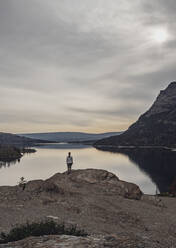 Einsame Frau steht vor einem unberührten und ruhigen See in den Bergen - CAVF74621