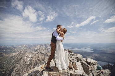 Ein frisch verheiratetes Paar küsst sich zum ersten Mal während der Hochzeit auf einem Berggipfel in Wyoming. - CAVF74636