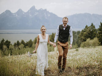 Bride and Groom walk through wildflower field in front of Mountains - CAVF74658