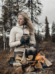 Young woman sitting by campfire - JOHF07723