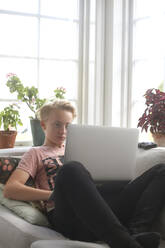 Boy on sofa using laptop - JOHF07770