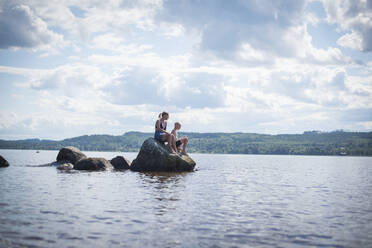 Mother and son sitting on rock at sea - JOHF07840