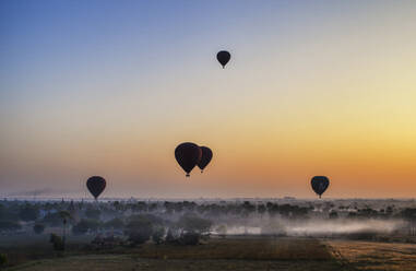 Heißluftballons über der Landschaft mit fernen Tempeln bei Sonnenuntergang, Bagan, Myanmar. - MINF13295