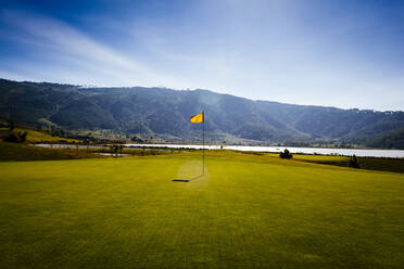 Flagge auf einem Golfplatz mit Meer und Bergen in der Ferne. - MINF13376