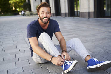 Porträt eines glücklichen Mannes, der in der Stadt auf dem Boden sitzt und seine Schuhe schnürt - PNEF02230