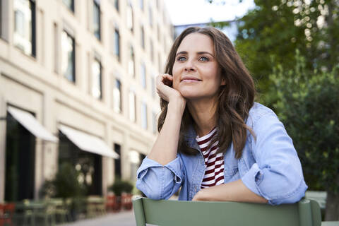 Portrait of smiling brunette woman sitting on a chair in the city stock photo