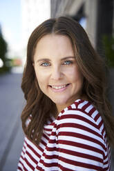 Portrait of smiling brunette woman in the city - PNEF02248