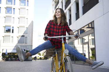 Happy brunette woman riding bicycle in the city - PNEF02255