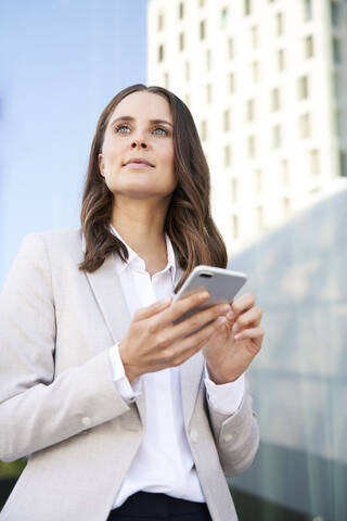 Porträt einer selbstbewussten Geschäftsfrau mit Mobiltelefon in der Stadt, lizenzfreies Stockfoto