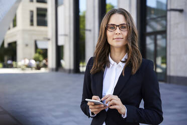 Portrait of confident businesswoman with cell phone in the city - PNEF02271