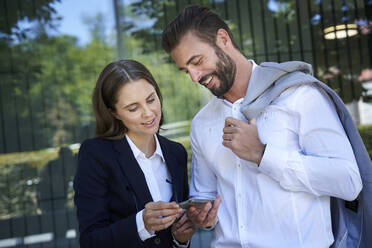 Businessman and businesswoman looking at cell phone in the city - PNEF02288