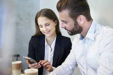 Geschäftsmann und Geschäftsfrau schauen auf ein Handy in einem Café - PNEF02291