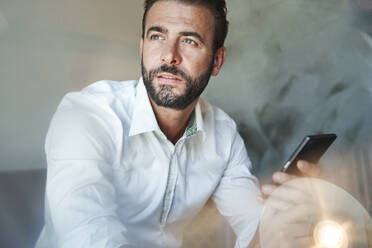 Porträt eines Geschäftsmannes mit weißem Hemd, der ein Mobiltelefon hält - PNEF02299