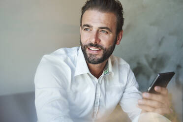 Portrait of smiling businessman wearing white shirt holding cell phone - PNEF02300