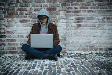 Teenager mit Laptop und auf einem Steinboden in der Stadt sitzend - ANHF00180