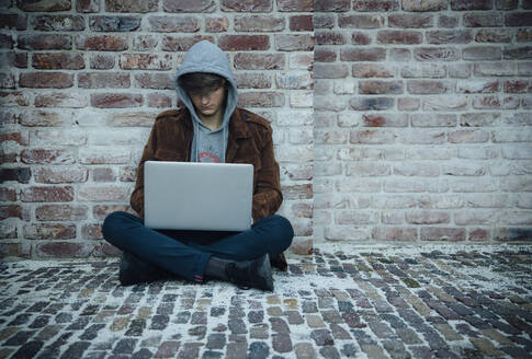 Teenager using laptop and sitting on a stone floor in the city - ANHF00180