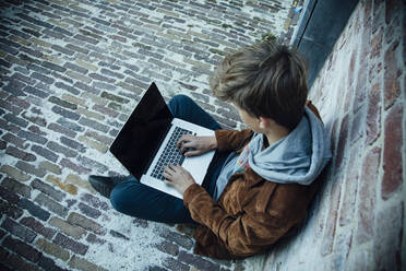 Teenager mit Laptop und auf einem Steinboden in der Stadt sitzend - ANHF00181