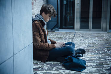 Teenager mit Laptop und auf einem Steinboden in der Stadt sitzend - ANHF00183