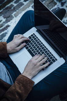 Teenager using laptop and sitting on a stone floor - ANHF00184