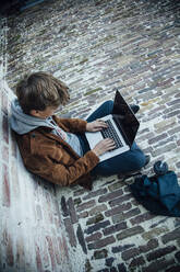 Teenager mit Laptop und auf einem Steinboden in der Stadt sitzend - ANHF00185