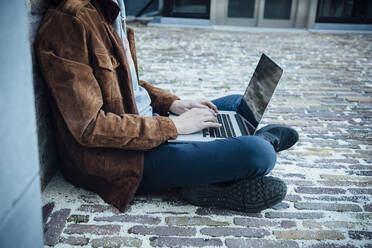 Teenager mit Laptop und auf einem Steinboden in der Stadt sitzend - ANHF00187