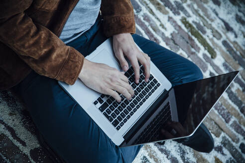 Teenager using laptop and sitting on a stone floor - ANHF00188