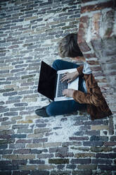 Teenager mit Laptop und auf einem Steinboden in der Stadt sitzend - ANHF00189