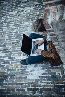Teenager using laptop and sitting on a stone floor in the city - ANHF00189