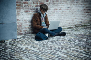 Teenager mit Laptop und auf einem Steinboden in der Stadt sitzend - ANHF00190