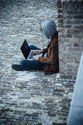 Teenager mit Laptop und auf einem Steinboden in der Stadt sitzend - ANHF00191