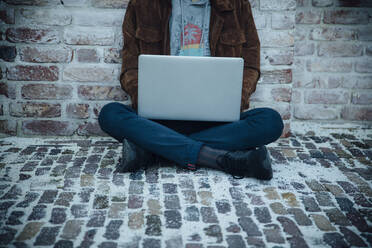 Teenager mit Laptop und auf einem Steinboden in der Stadt sitzend - ANHF00192