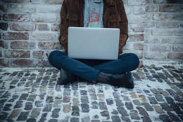 Teenager using laptop and sitting on a stone floor in the city - ANHF00192